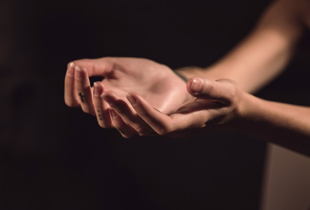 Mâinile unei persoane care se roagă, cerând îndurare de la divinitate, și care are o cruce tatuată pe deget
