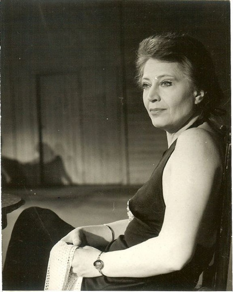 Gina Patrichi pe un scaun, ținând o bucată de dantelă albă în mână.