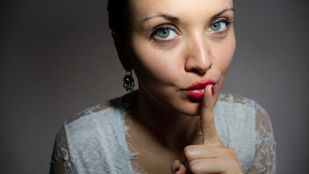 Imagine cu o femeie care ține degetul la gură și arată semnul tăcerii 