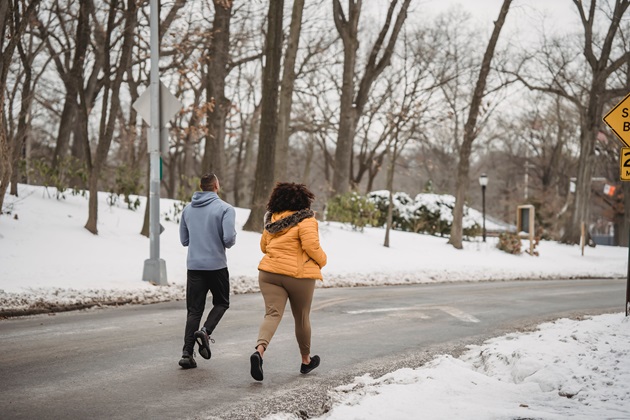 O femeie si un barbat care aleargă pe stradă, în timpul iernii