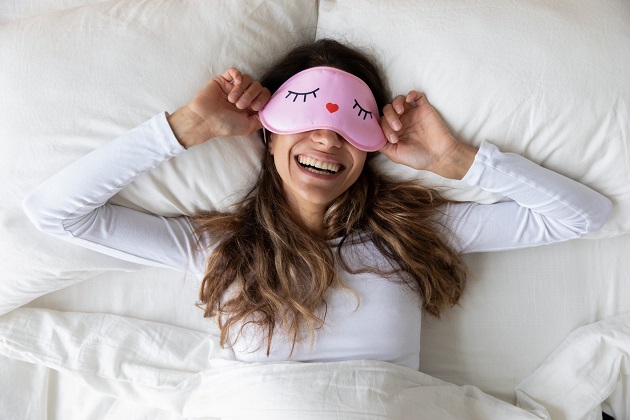 femeie in pat pregatita de culcare care isi trage masca de dormit pe ochi