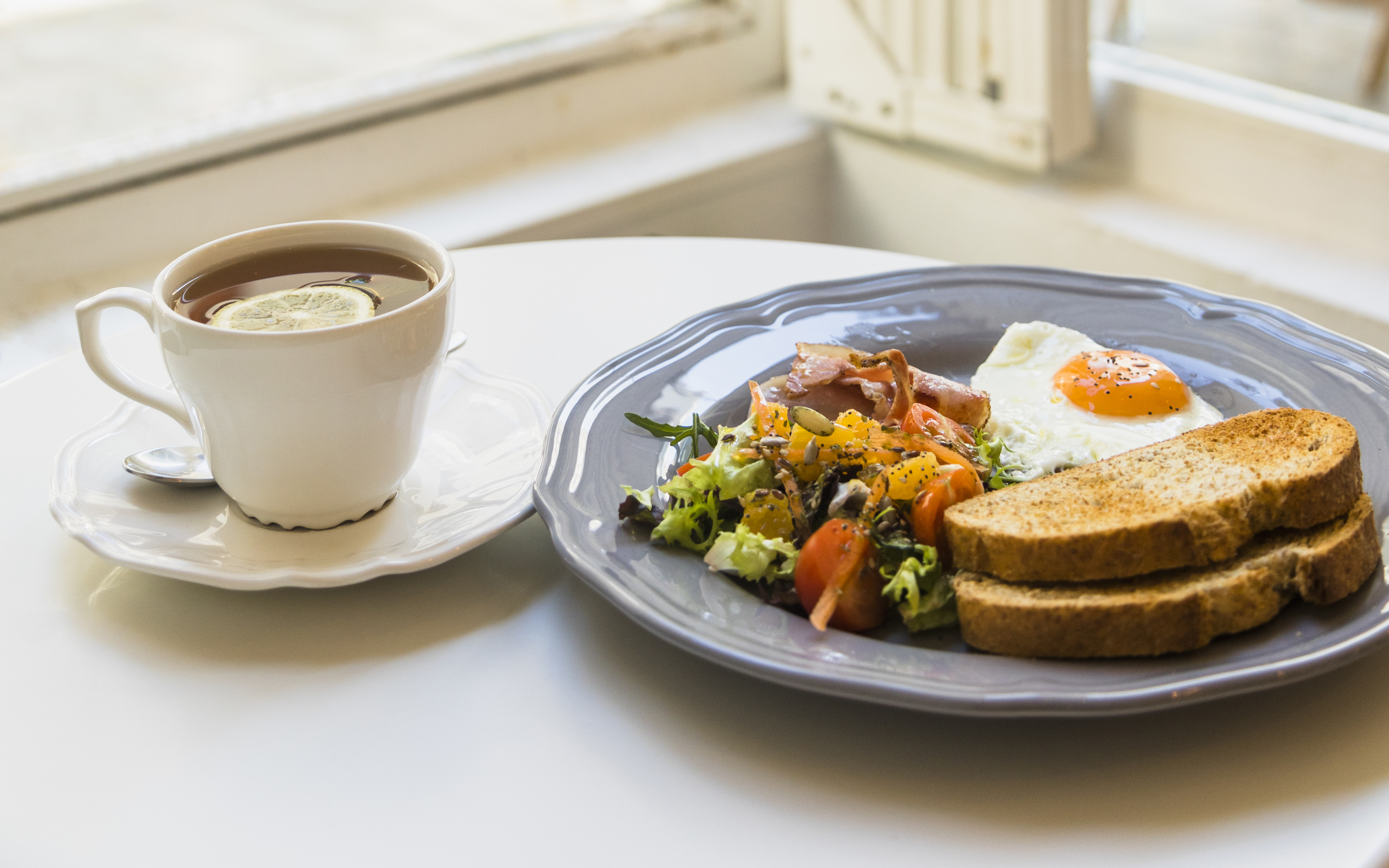 Mic dejun, farfurie cu alimente și o ceașcă de ceai lângă o fereastră prin care intră razele de soare