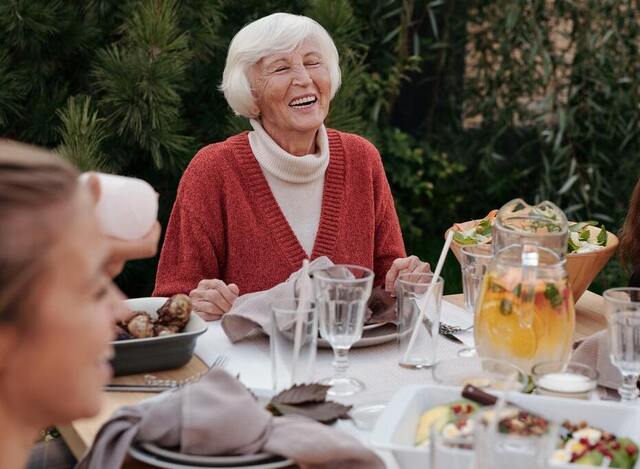Femeie în vârstă care mănâncă la masă și râde