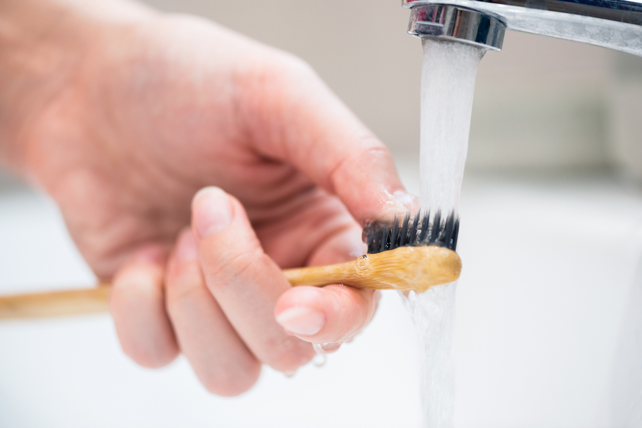 Persoană care își spală cu apă de la robinet periuța de dinți.