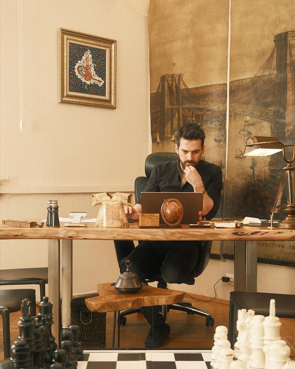 Tuncay Ozturk în biroul său, cu privirea în laptop, ținându-și mâna la barbă