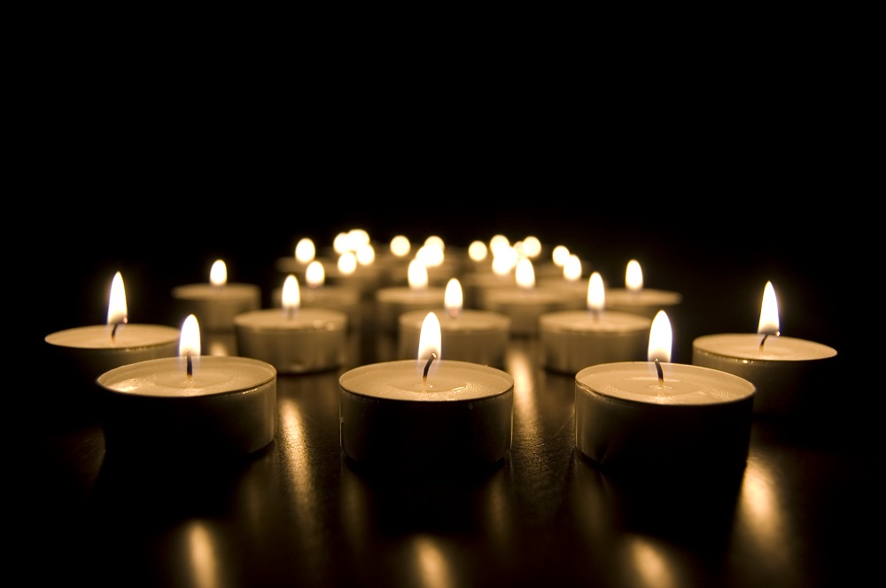 Multe lumânări aprinse, așezate una lângă alta în întuneric