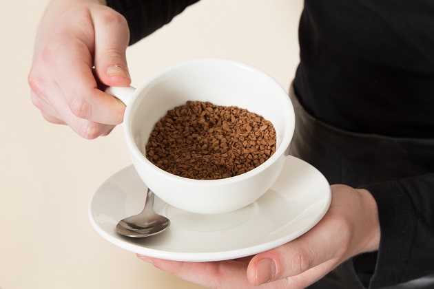 Persoană care ține în mână o ceașcă umplută pe jumătate cu granule de cafea solubilă