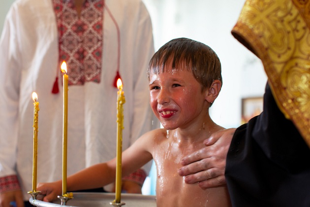 Copil introdus de preot în cristelniță în timp ce primește botezul într-o biserică ortodoxă