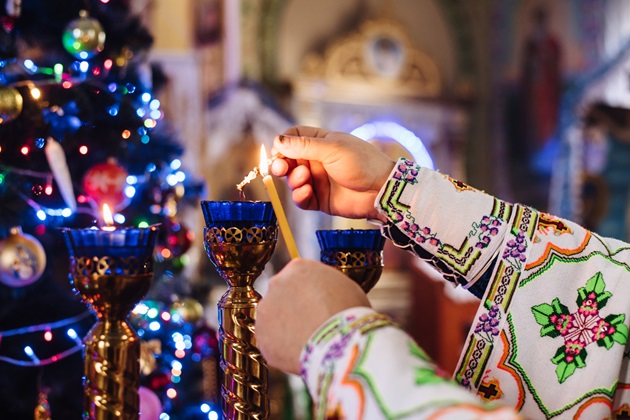Preot care aprinde candele în biserică, lângă bradul de Crăciun
