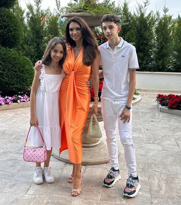 Cristina Spătar într-o rochie portocalie, alături de cei doi copii ai săi, amândoi îmbrăcați în alb