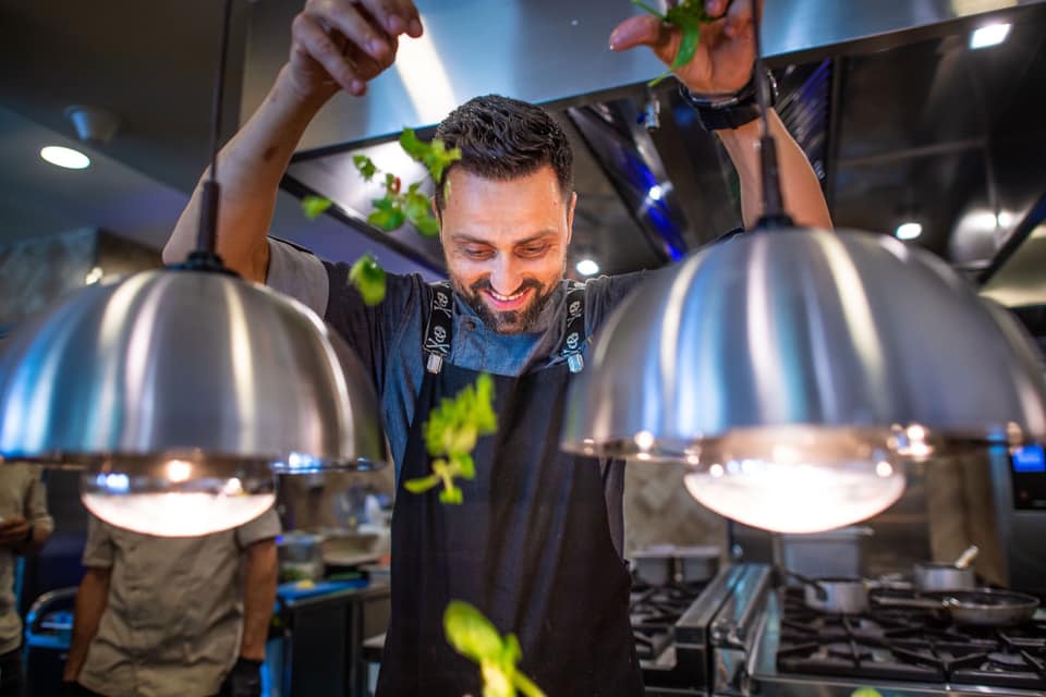 Chef Orlando Zaharia în bucătărie, în timp ce adaugă verdeață peste preparatele sale, folosindu-se de ambele mâini