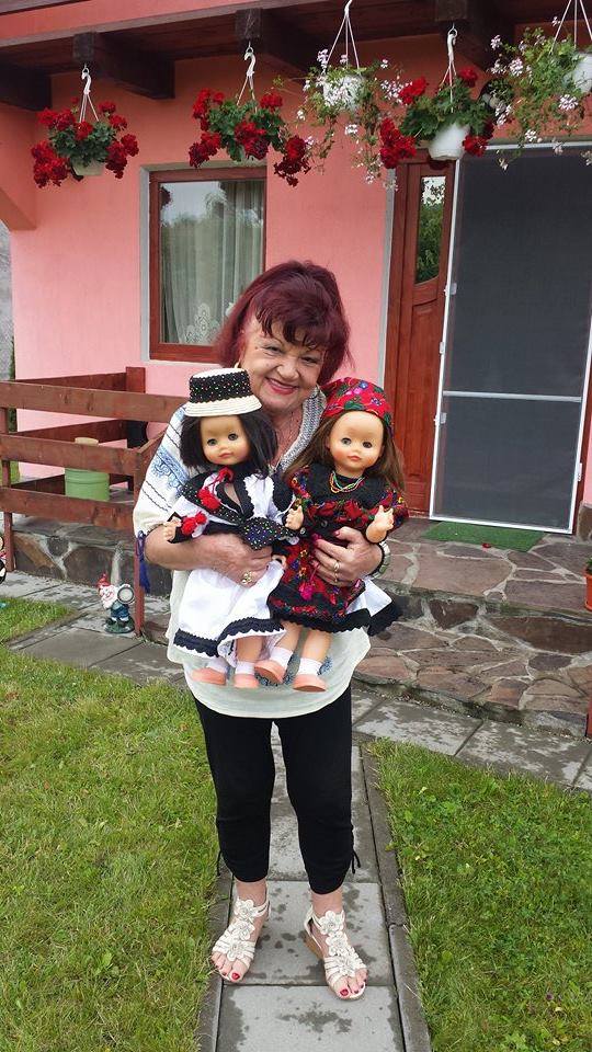 Florentina Satmari în fața casei sale din Mureș, ținând două păpuși în brațe