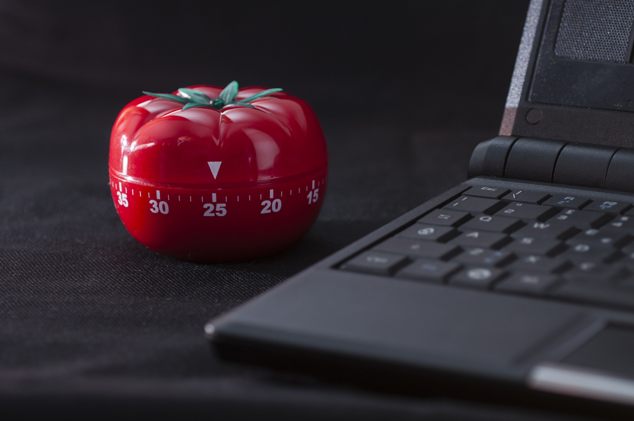 laptop alături de un timer în formă de roșie, așezat pe o masă acoperită cu un material bleumarin