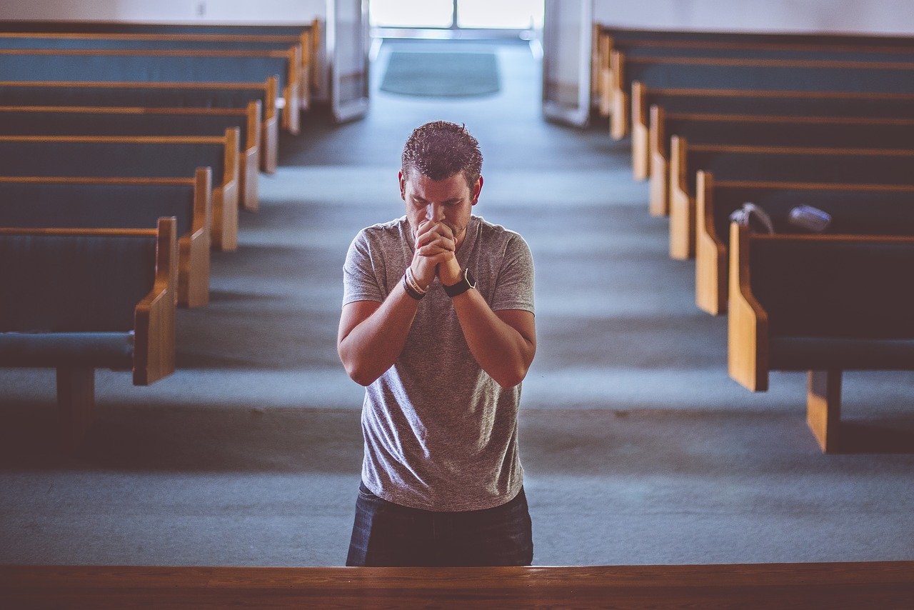 tânăr aflat într-o biserică goală unde se roagă în genunchi
