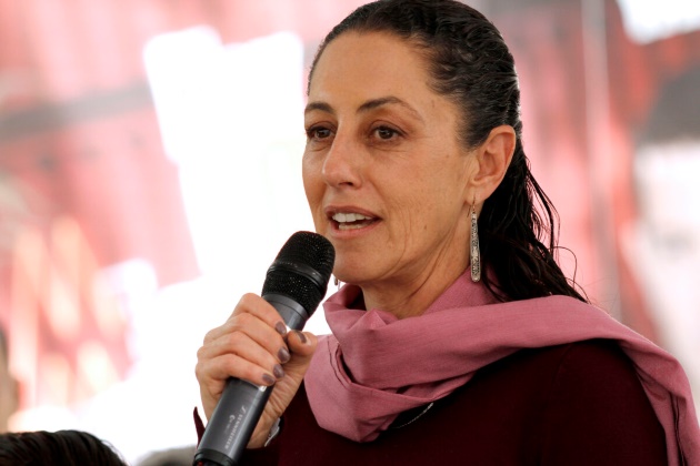 claudia sheinbaum cu o bluza neagra si o esarfa roz vorbeste in microfon la un eveniment