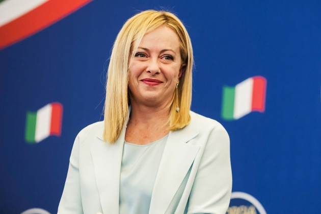 giorgia meloni imbracata cu un costum alb zambeste la o conferinta de presa