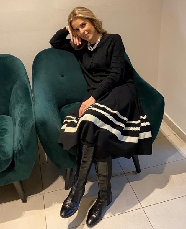cristela georgescu imbracata cu o rochie eleganta neagra pozeaza pe un fotoliu verde inchis