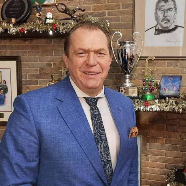helmuth dukadam in costum albastru pozeaza in fata semineului, alaturi de un portret si un trofeu 