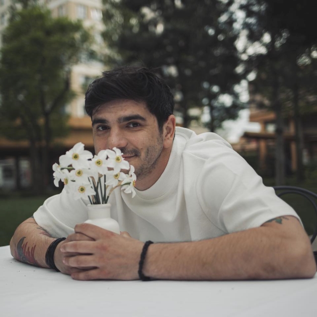 alex bogdan imbracat intr-un tricou alb in aer liber tine un buchet de narcise
