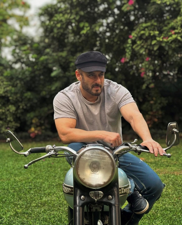 salman khan pozand pe o motocicleta imbracat cu un tricou lejer si sapca