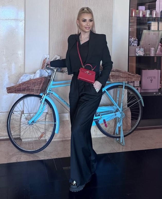 impresara anamaria prodan pozeaza intr-un costum negru, elegant in fata unei biciclete