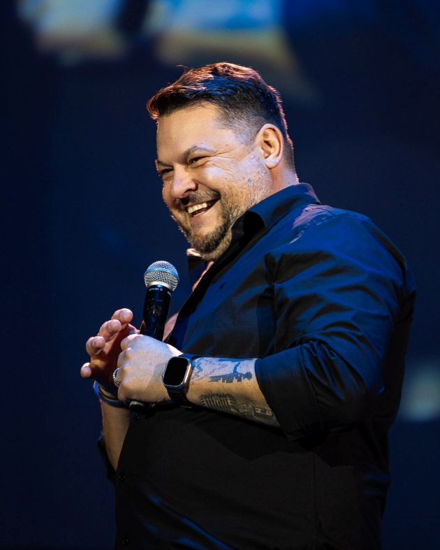 mihai bobonete imbracat cu camasa rade pe scena in timpul unui show de stand-up