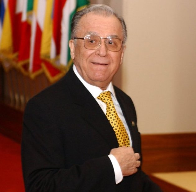 ion iliescu imbracat in costum negru cu cravata galbena se uita catre camera
