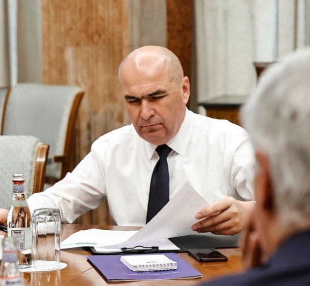 ilie bolojan imbracat cu camasa alba si cravata neagra studiaza documente