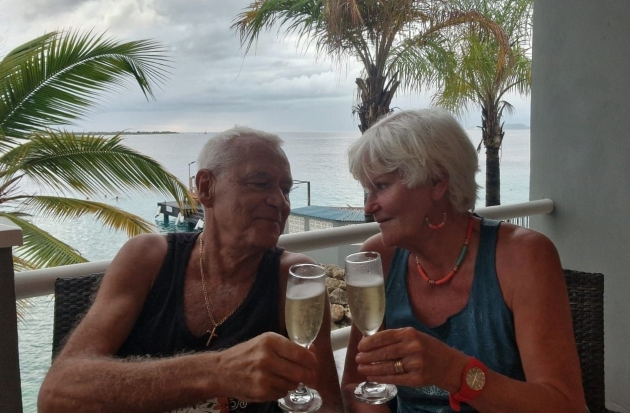 victor si monica tatoiu imbracati cu haine subtiri de vara ciocnesc un pahar de sampanie in vacanta