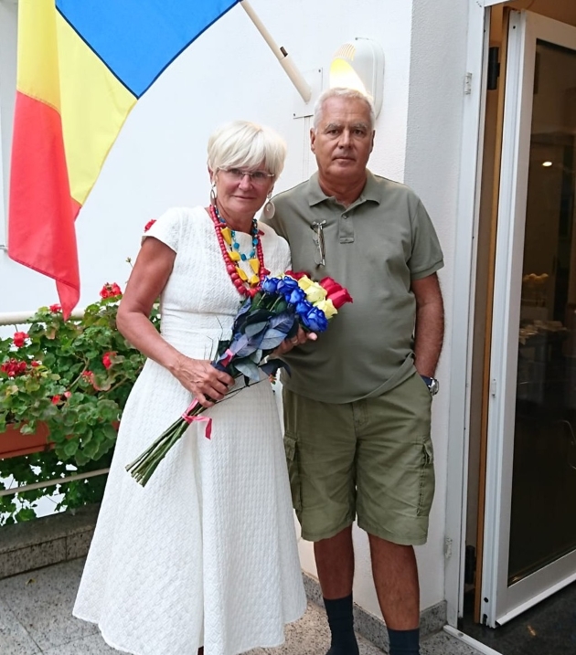 monica si victor tatoiu imbracati casual pozeaza in fata tricolorului cu un buchet de trandafiri tricolor
