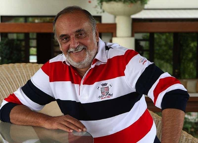 dinu patriciu fotografiat zambind in timp ce poarta un tricou polo cu dungi