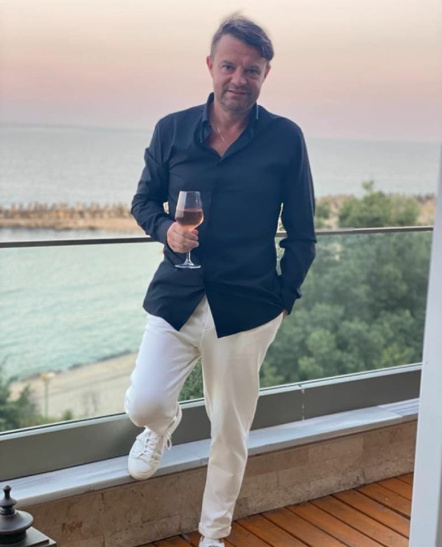 Andrei Duban în pantaloni albi și cămașă albă bea un pahar cu vin
