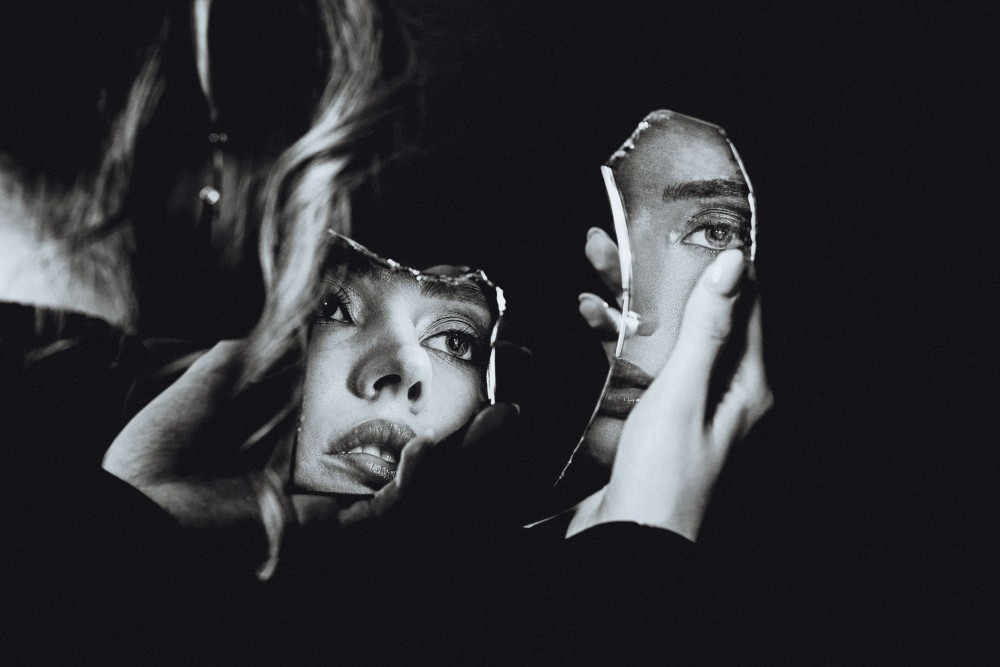 Fotografie alb negru cu o femeie care se uită într-o oglindă spartă