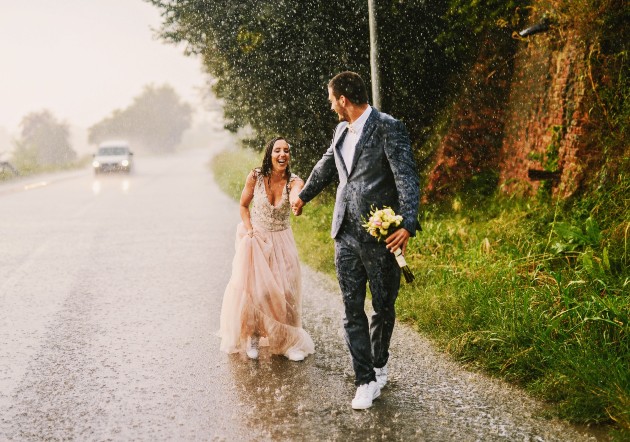 Imagine cu o mireasă și un mire în mijlocul străzii alergțnd prin ploaie
