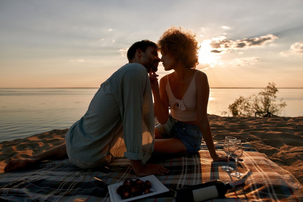 Imagine cu o femeie și un bărbat care stau pe plajă și se sărută