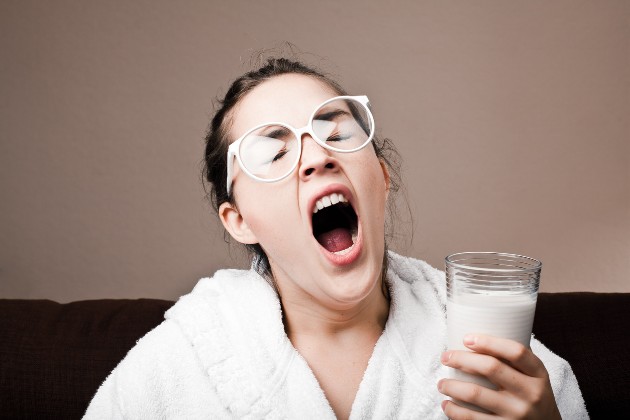 Imagine cu o femeie care ține un pahar cu lapte în mână și cască