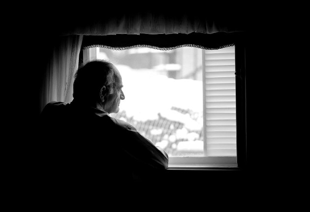 Imagine alb-negru cu un bărbat în vârstă care se uită pe geam