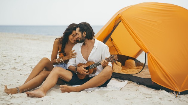 Imagine cu o femeie și un bărbat care stau pe plajă lângă un cort galben