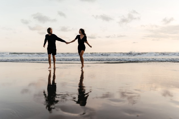 Imagine cu o femeie și un bărbat care se țin de mână pe plajă