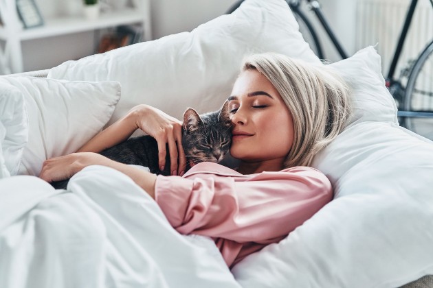 Imagine cu o femeie care stă în pat și îmbrățișează o pisică