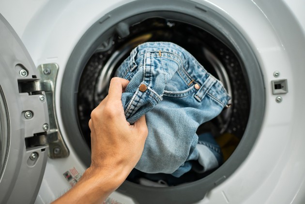 Imagine cu o mână care pune o pereche de blugi în mașina de spălat