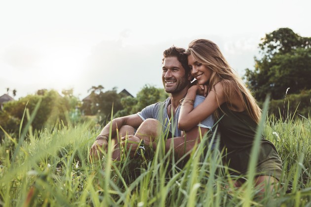 Imagine cu o femeie și un bărbat fericiți care stau în iarbă