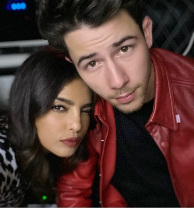 Imagine cu Nick Jonas în cămașă roșie și Priyanka Chopra care face cu ochiul