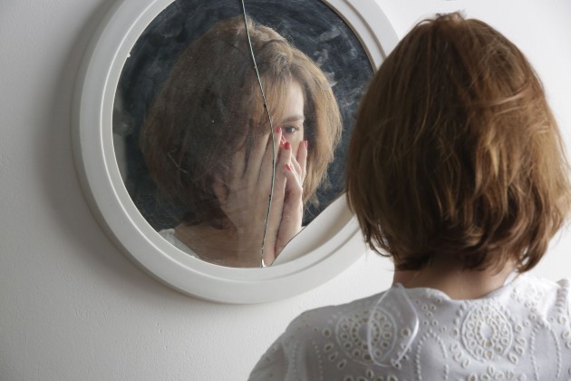Imagine cu o femeie care se uită într-o oglindă spartă
