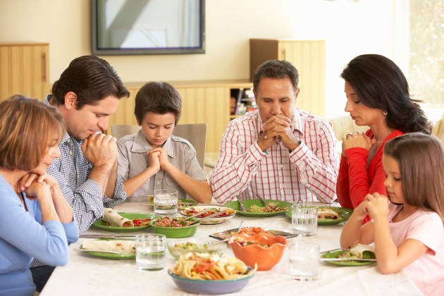 Imagine cu o familie care stă în jurul mesei și se roagă