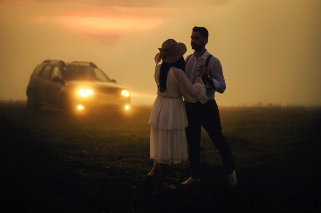 Imagine cu o femeie și un bărbat care dansează lângă o mașină, pe câmpie