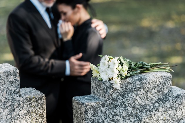 Imagine cu un bărbat și o femeie ce se țin în brațe lângă mormânt