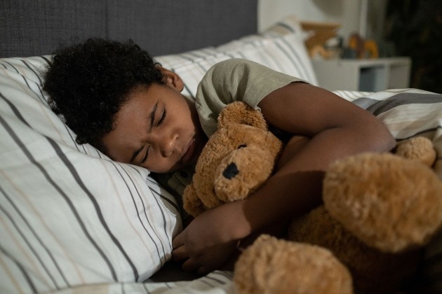 Imagine cu un băiat negru care doarme cu un ursuleț în brațe