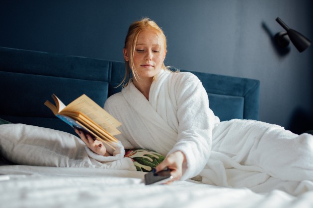 Imagine cu o femeie blondă care stă în pat într-un halat alb