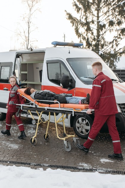 Imagine cu o ambulanță și doi medici care transportă o femeie pe targă